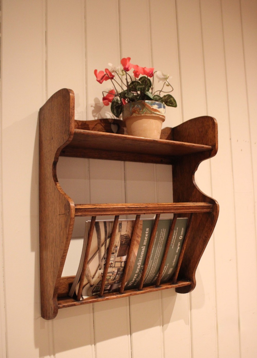 An Arts and Crafts solid oak wall shelf featuring a top shelf ledge with a pierced heart cutout and a lower magazine rack with vertical wooden spindles. View XI