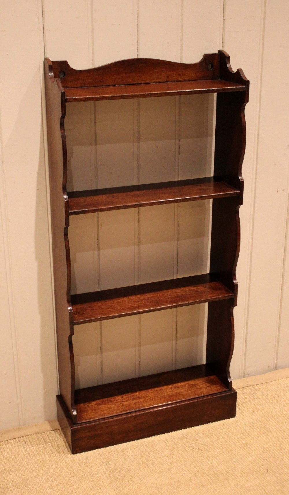 A small dark oak open bookcase featuring four tier shelves, shaped side panels, and a scrolled top gallery.