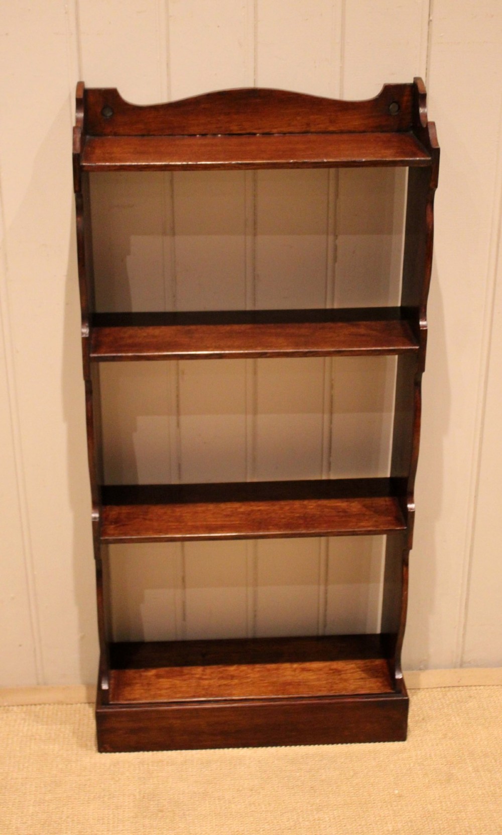 A small dark oak open bookcase featuring four tier shelves, shaped side panels, and a scrolled top gallery. View IV