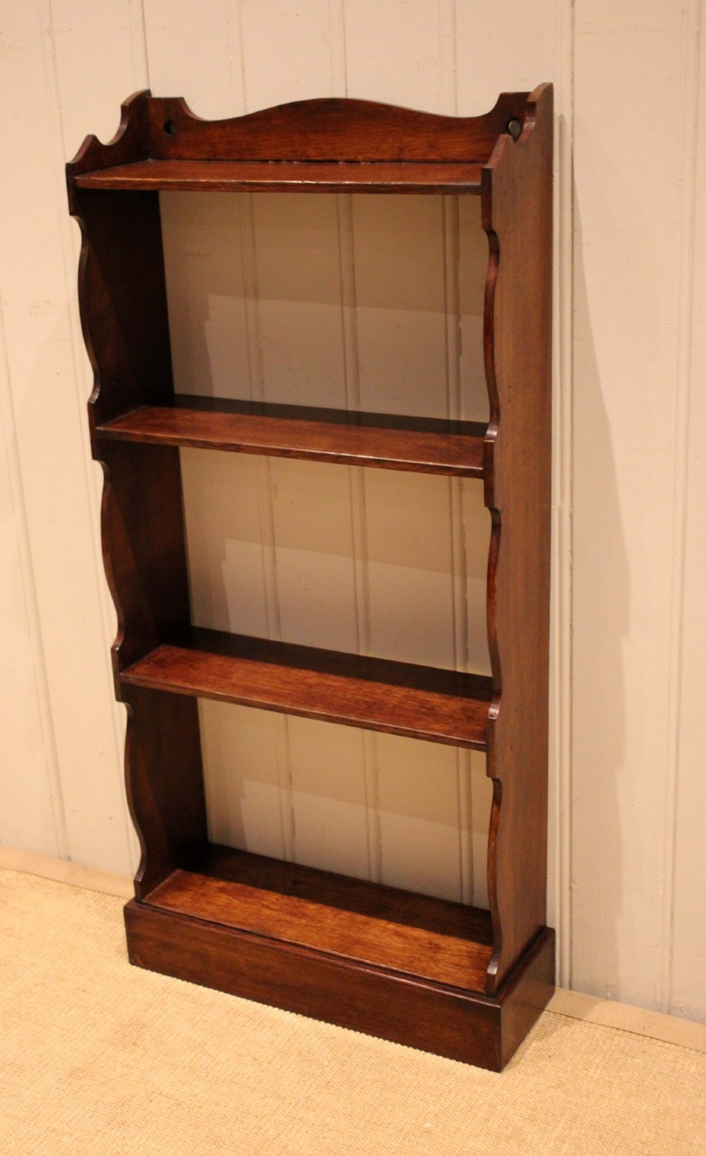 A small dark oak open bookcase featuring four tier shelves, shaped side panels, and a scrolled top gallery. View VI