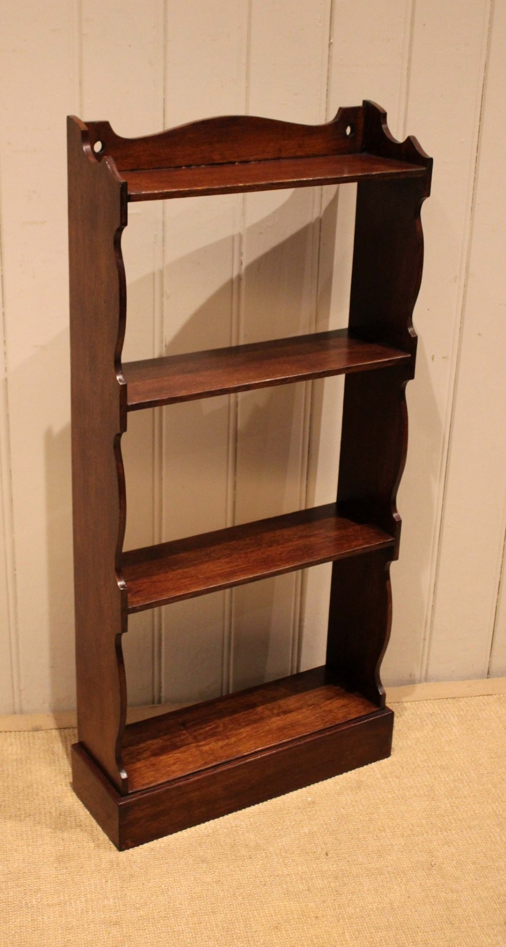 A small dark oak open bookcase featuring four tier shelves, shaped side panels, and a scrolled top gallery. View X