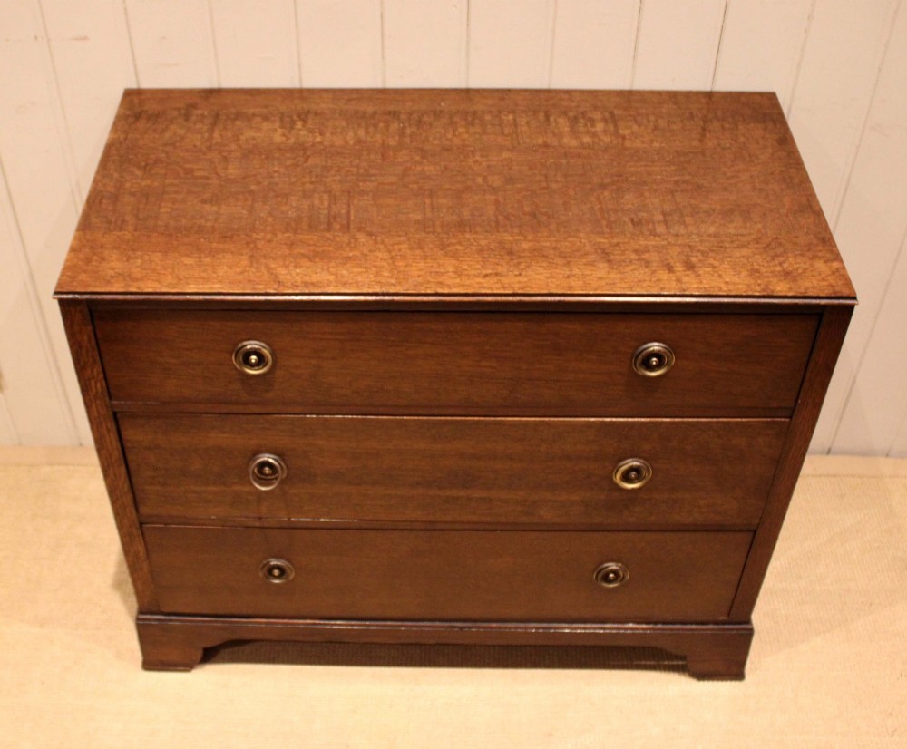 An early 20th-century medium brown oak chest of drawers with three drawers, circular brass ring handles, and bracket feet.