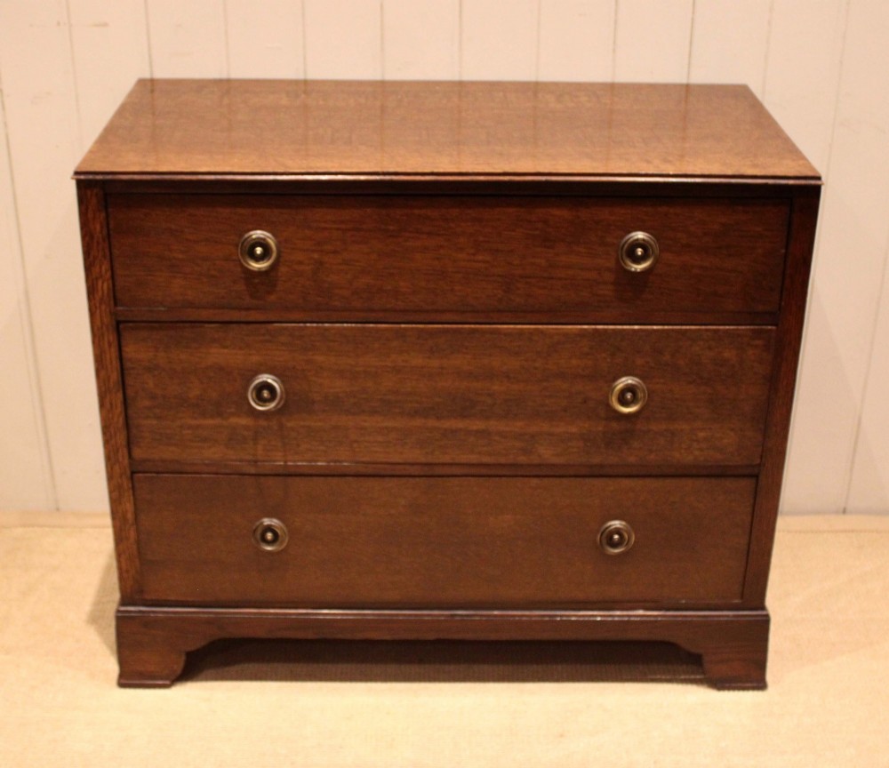 An early 20th-century medium brown oak chest of drawers with three drawers, circular brass ring handles, and bracket feet. View II