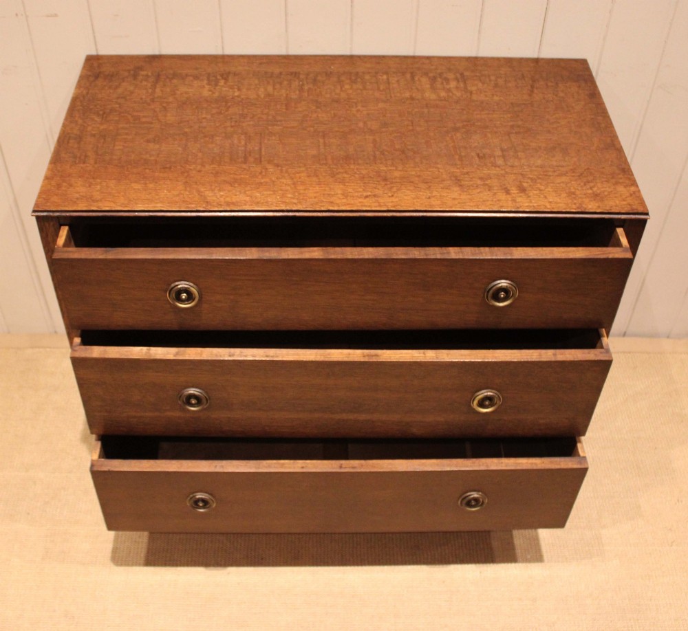 An early 20th-century medium brown oak chest of drawers with three drawers, circular brass ring handles, and bracket feet. View IV