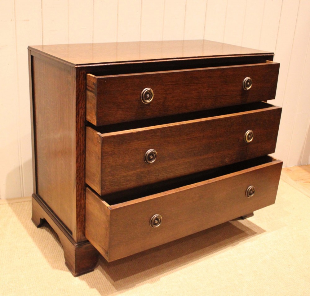 An early 20th-century medium brown oak chest of drawers with three drawers, circular brass ring handles, and bracket feet. View V
