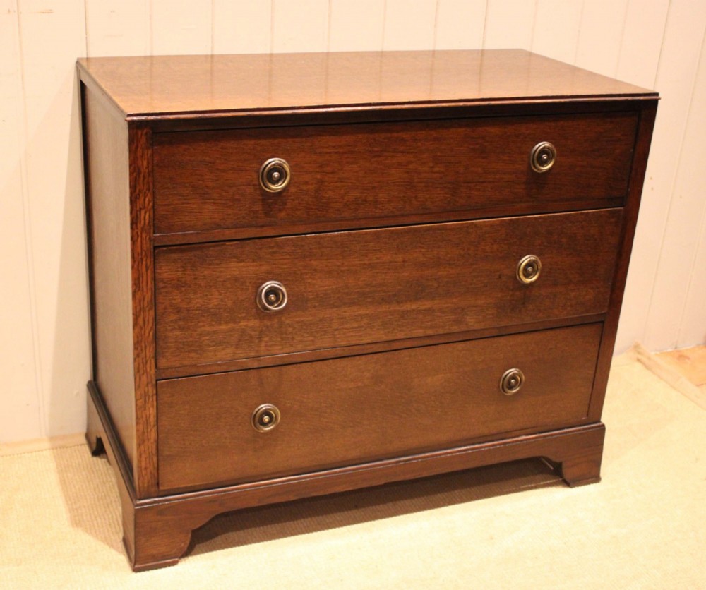 An early 20th-century medium brown oak chest of drawers with three drawers, circular brass ring handles, and bracket feet. View VI