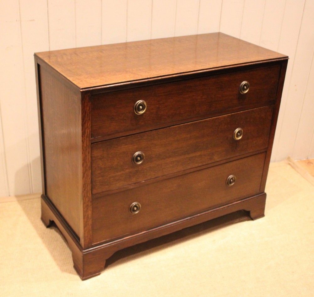 An early 20th-century medium brown oak chest of drawers with three drawers, circular brass ring handles, and bracket feet. View VII