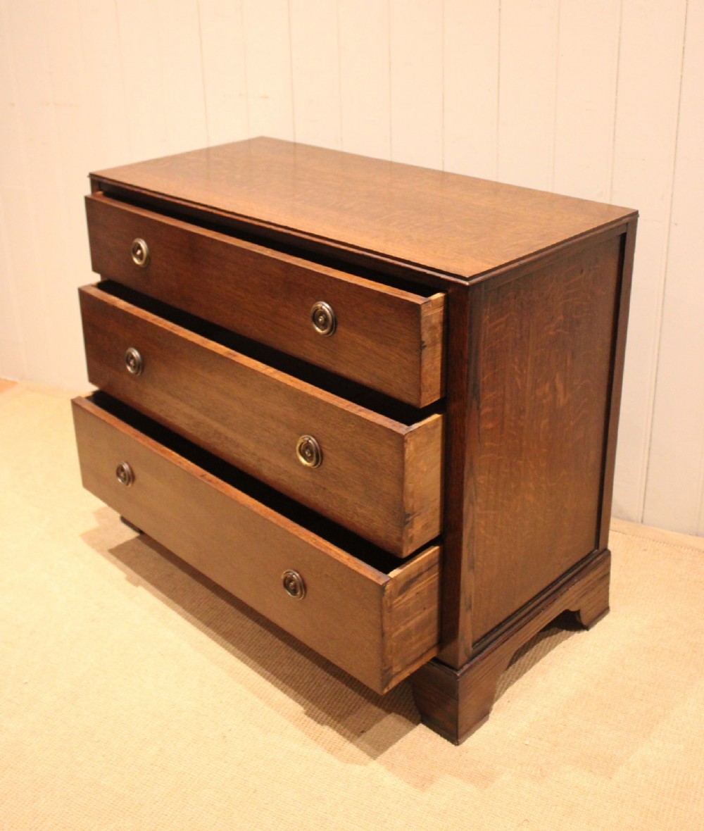 An early 20th-century medium brown oak chest of drawers with three drawers, circular brass ring handles, and bracket feet. View VIII