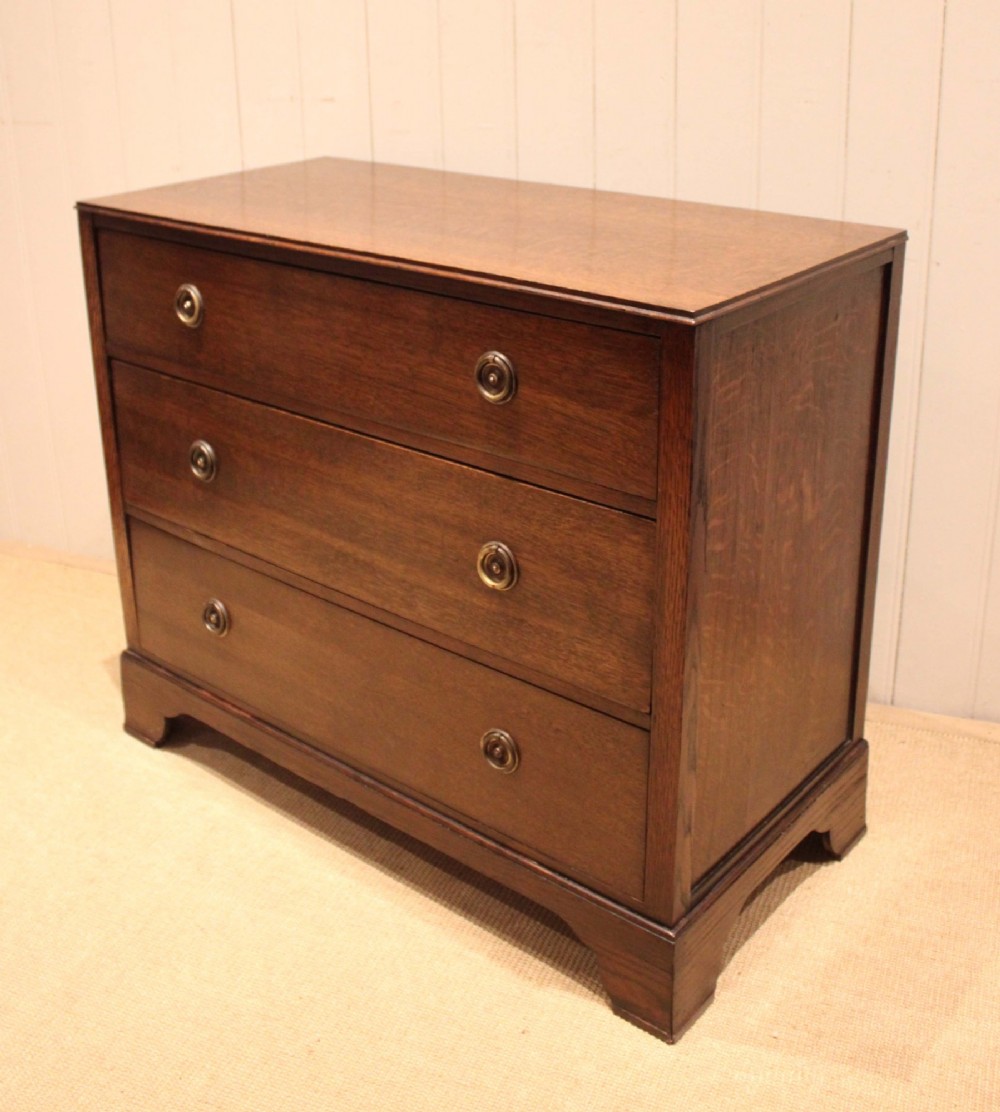 An early 20th-century medium brown oak chest of drawers with three drawers, circular brass ring handles, and bracket feet. View IX
