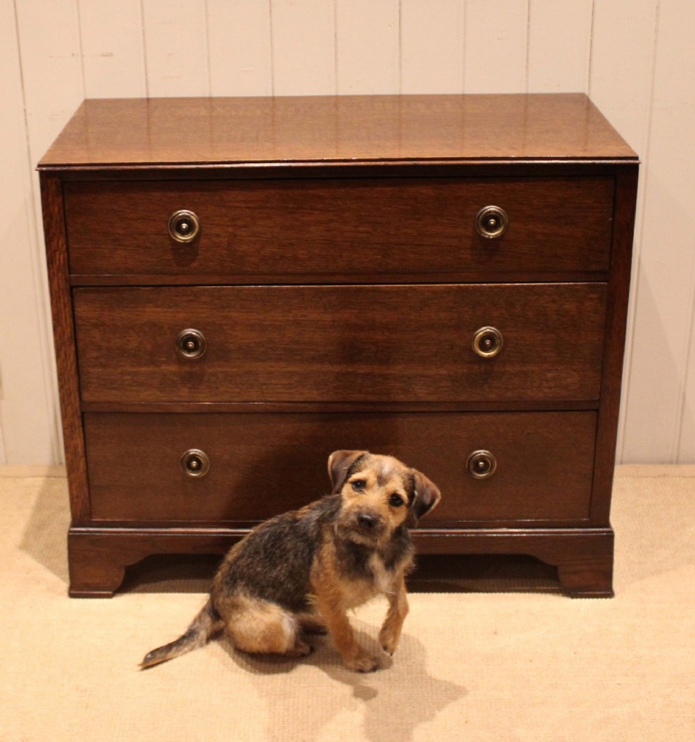 An early 20th-century medium brown oak chest of drawers with three drawers, circular brass ring handles, and bracket feet. View X