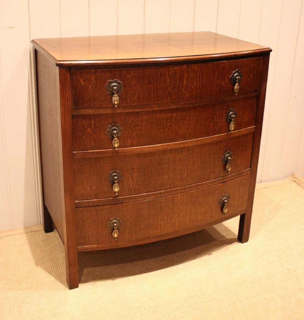A dark oak chest of drawers featuring a curved bowfront facade and four graduated drawers with antique brass pendant handles. View II