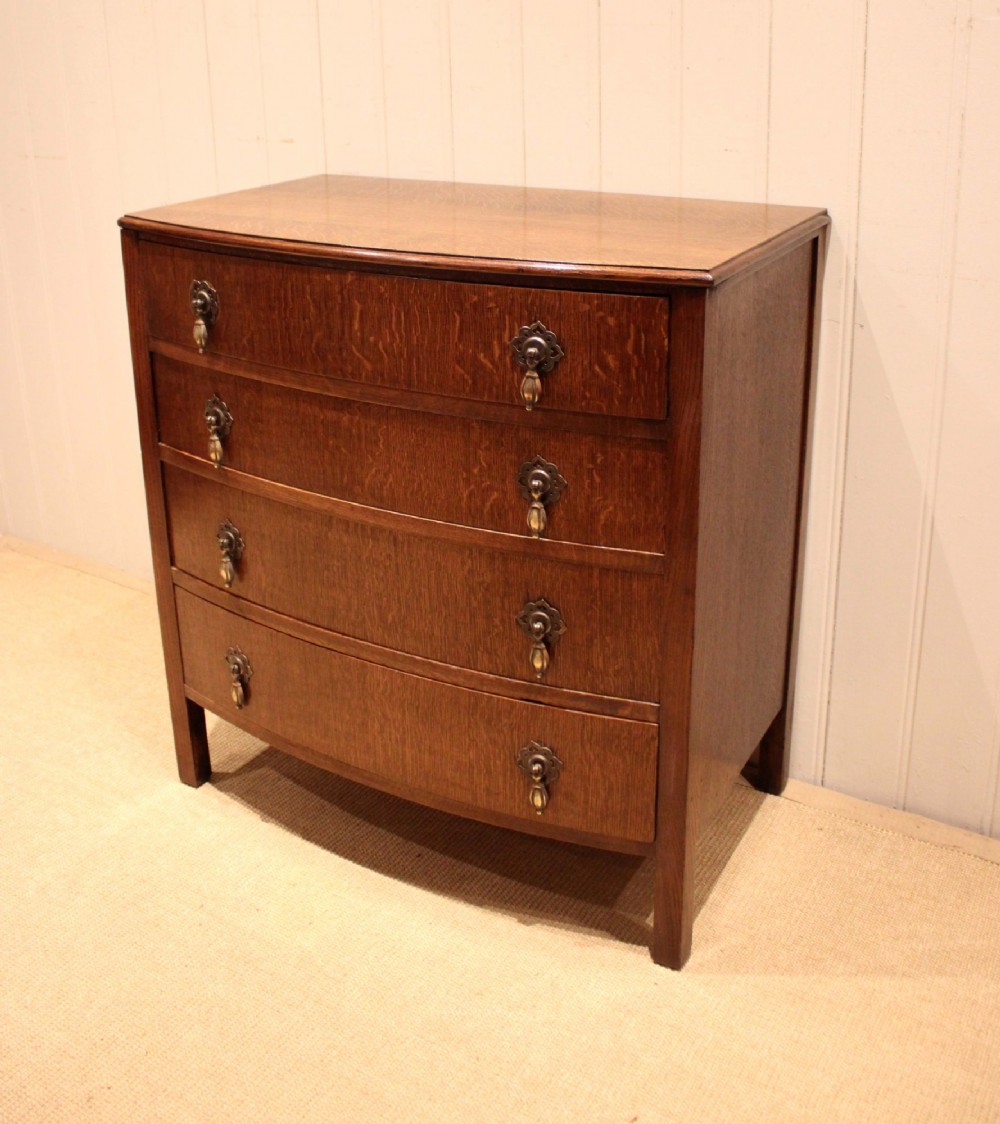 A dark oak chest of drawers featuring a curved bowfront facade and four graduated drawers with antique brass pendant handles. View III