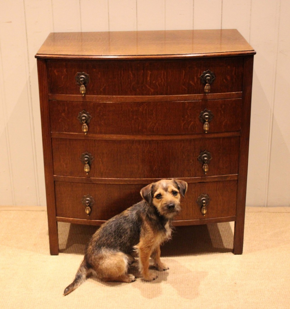 A dark oak chest of drawers featuring a curved bowfront facade and four graduated drawers with antique brass pendant handles. View VIII