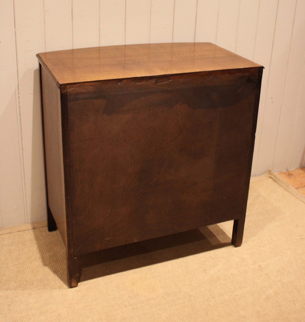 A dark oak chest of drawers featuring a curved bowfront facade and four graduated drawers with antique brass pendant handles. View XII