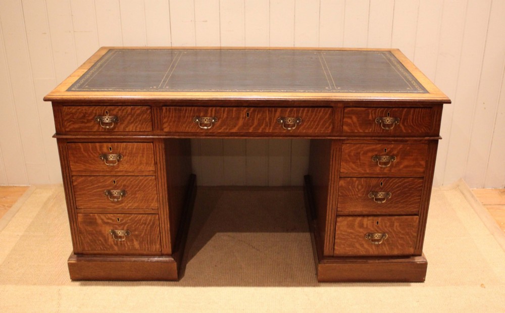 An Edwardian figured oak pedestal desk featuring a dark green leather writing surface and nine drawers with brass handles.