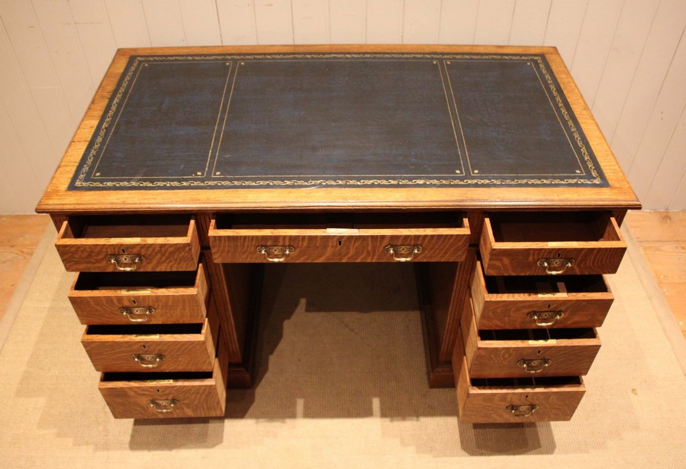 An Edwardian figured oak pedestal desk featuring a dark green leather writing surface and nine drawers with brass handles. View III