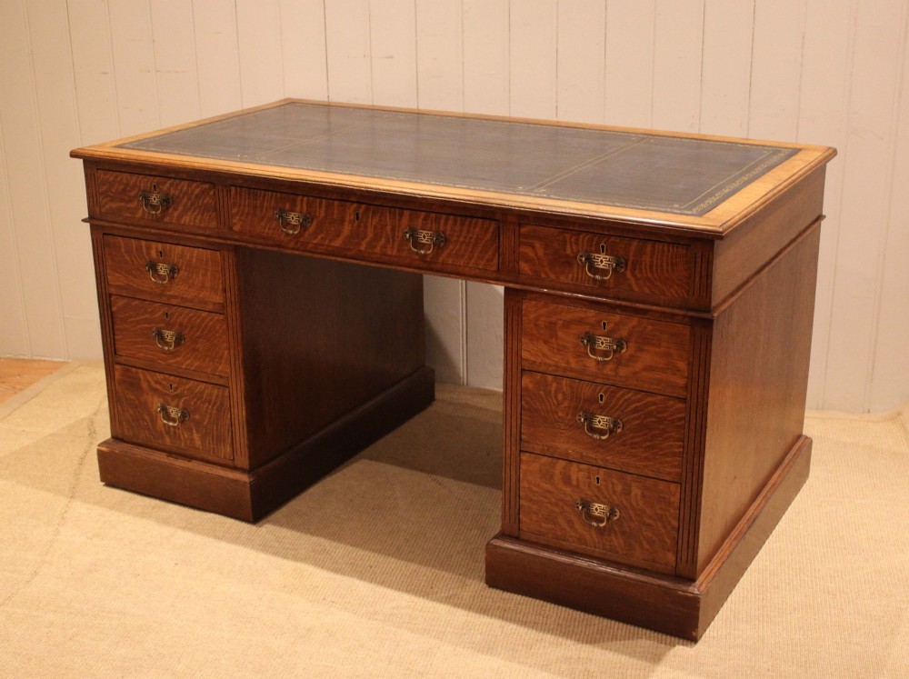 An Edwardian figured oak pedestal desk featuring a dark green leather writing surface and nine drawers with brass handles. View V