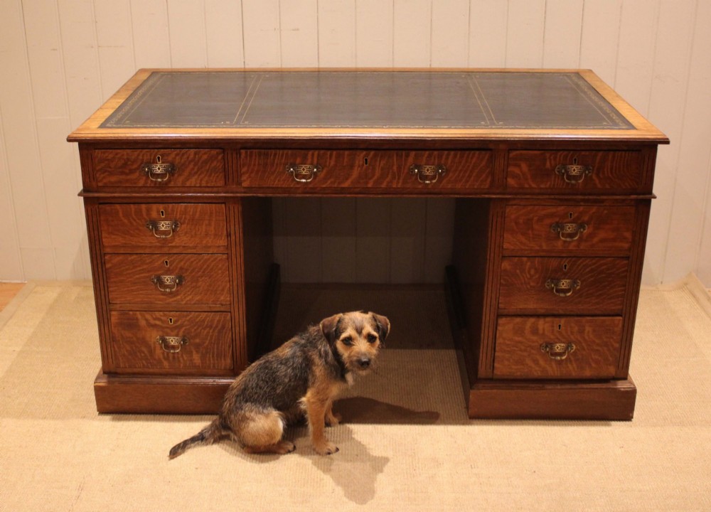 An Edwardian figured oak pedestal desk featuring a dark green leather writing surface and nine drawers with brass handles. View VI