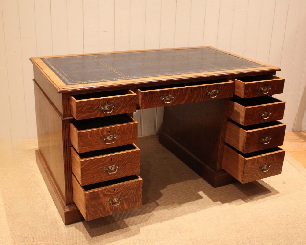 An Edwardian figured oak pedestal desk featuring a dark green leather writing surface and nine drawers with brass handles. View VII