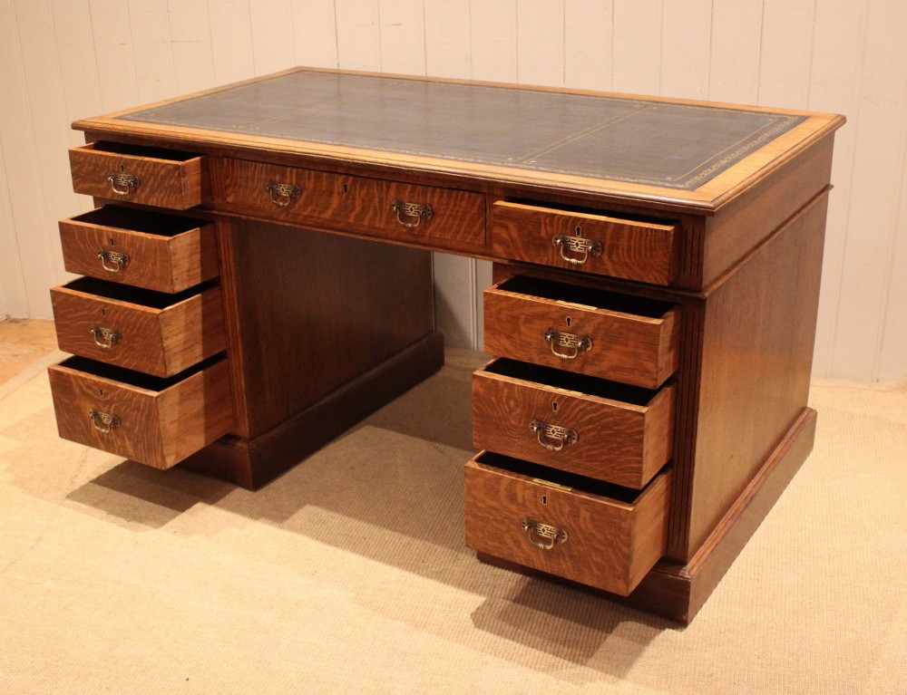 An Edwardian figured oak pedestal desk featuring a dark green leather writing surface and nine drawers with brass handles. View VIII
