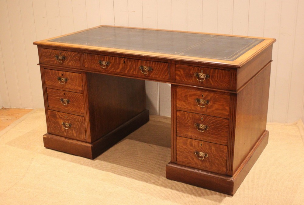 An Edwardian figured oak pedestal desk featuring a dark green leather writing surface and nine drawers with brass handles. View IX