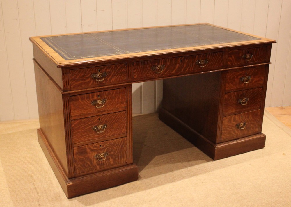 An Edwardian figured oak pedestal desk featuring a dark green leather writing surface and nine drawers with brass handles. View X
