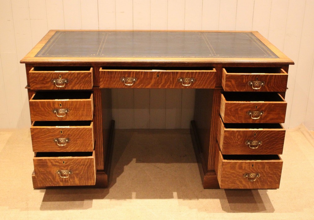 An Edwardian figured oak pedestal desk featuring a dark green leather writing surface and nine drawers with brass handles. View XI