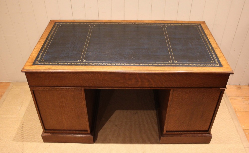 An Edwardian figured oak pedestal desk featuring a dark green leather writing surface and nine drawers with brass handles. View XIII