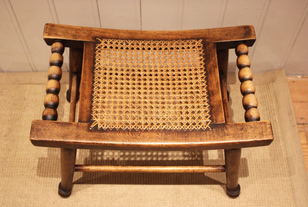 An antique warm brown beechwood stool featuring a woven cane seat, bobbin-turned side handles, and splayed turned legs. View VIII