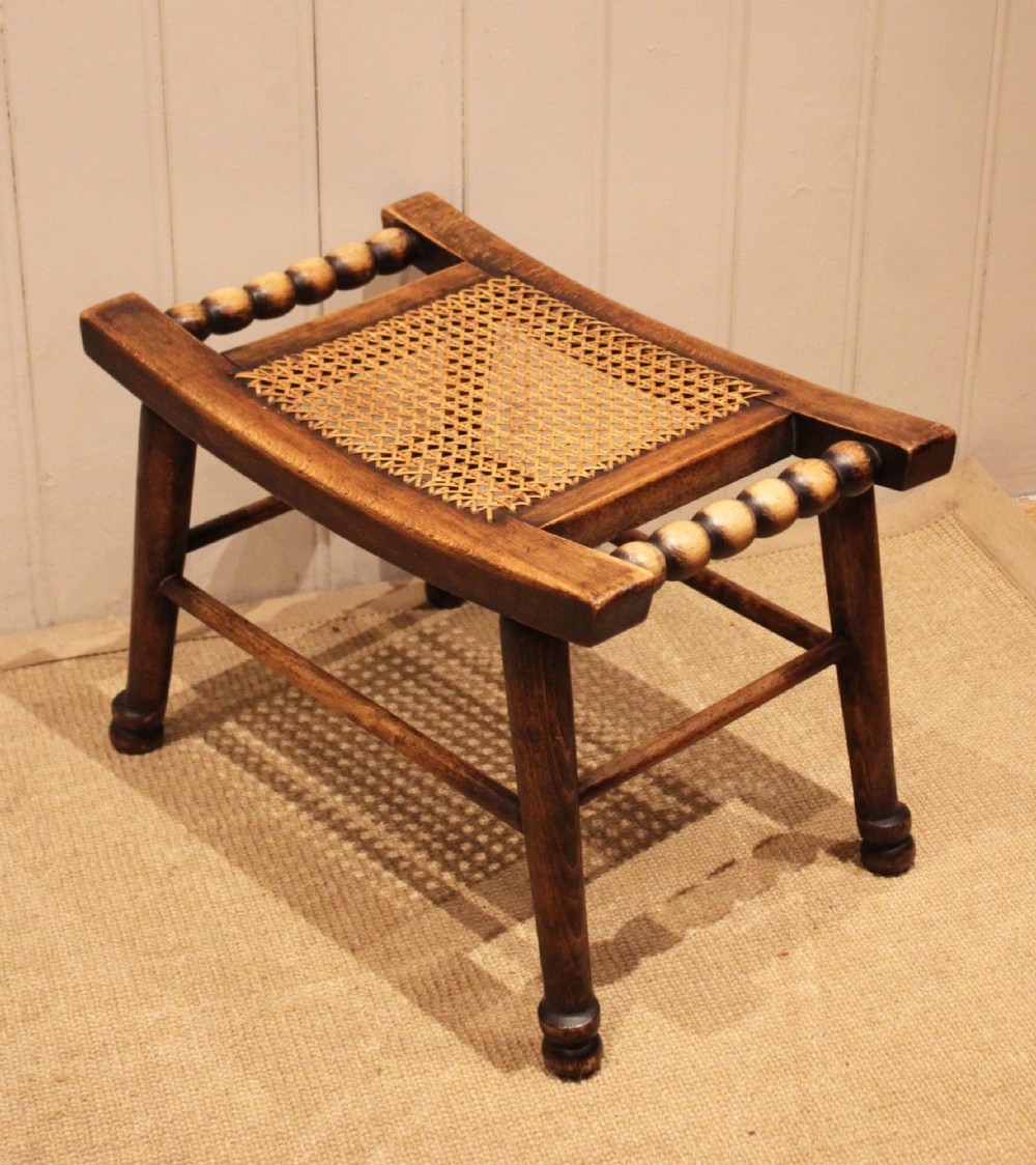 An antique warm brown beechwood stool featuring a woven cane seat, bobbin-turned side handles, and splayed turned legs. View XI