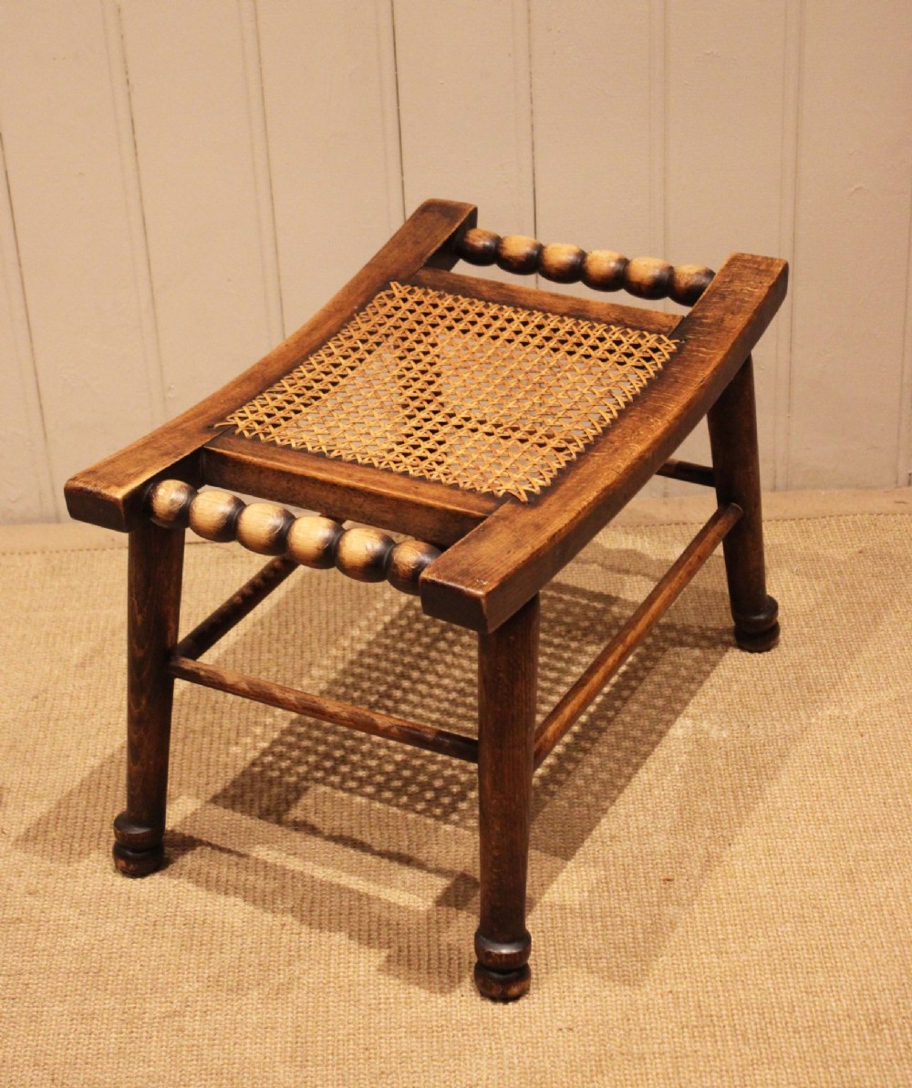 An antique warm brown beechwood stool featuring a woven cane seat, bobbin-turned side handles, and splayed turned legs. View XII