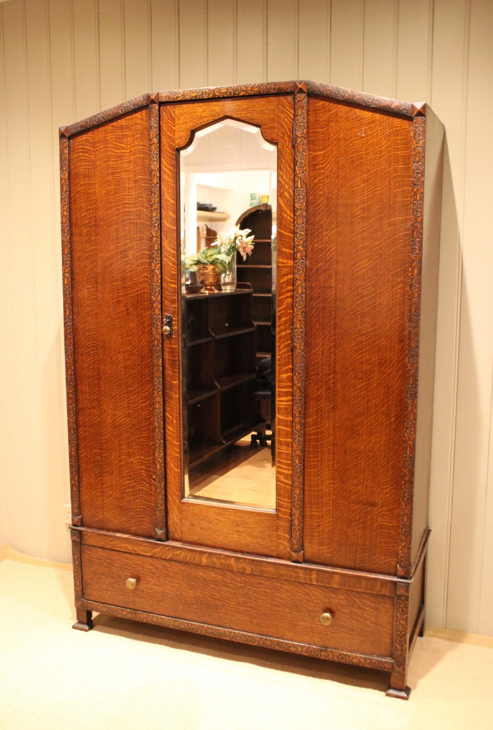 An early twentieth-century warm brown oak wardrobe with a central arched mirror door, carved foliate border mouldings, and a single lower drawer. View II
