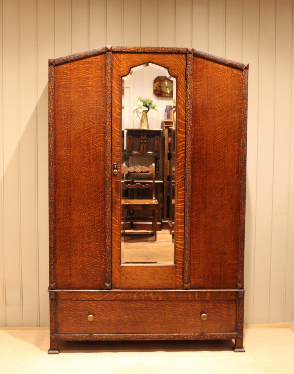 An early twentieth-century warm brown oak wardrobe with a central arched mirror door, carved foliate border mouldings, and a single lower drawer. View III
