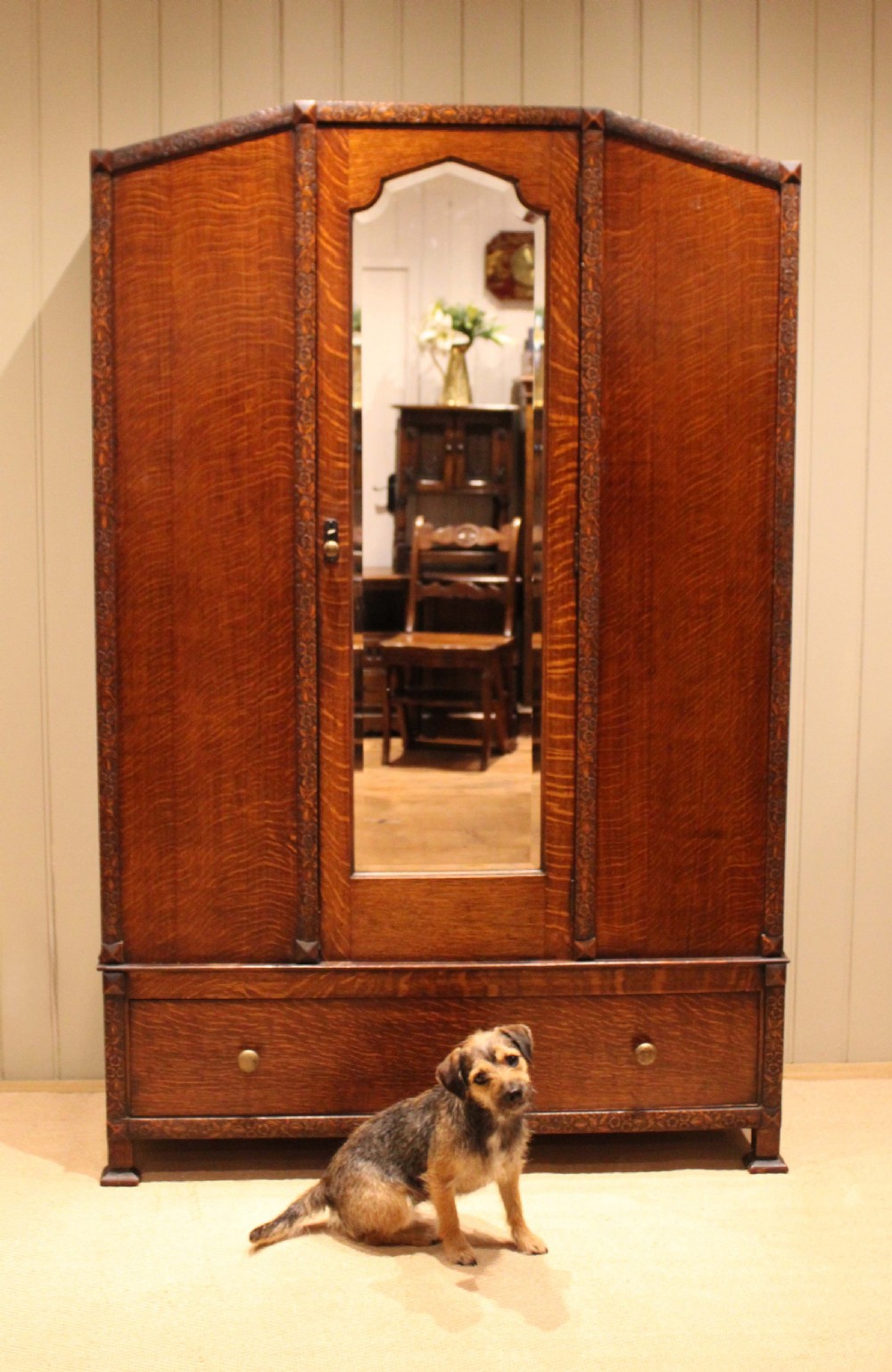 An early twentieth-century warm brown oak wardrobe with a central arched mirror door, carved foliate border mouldings, and a single lower drawer. View IV