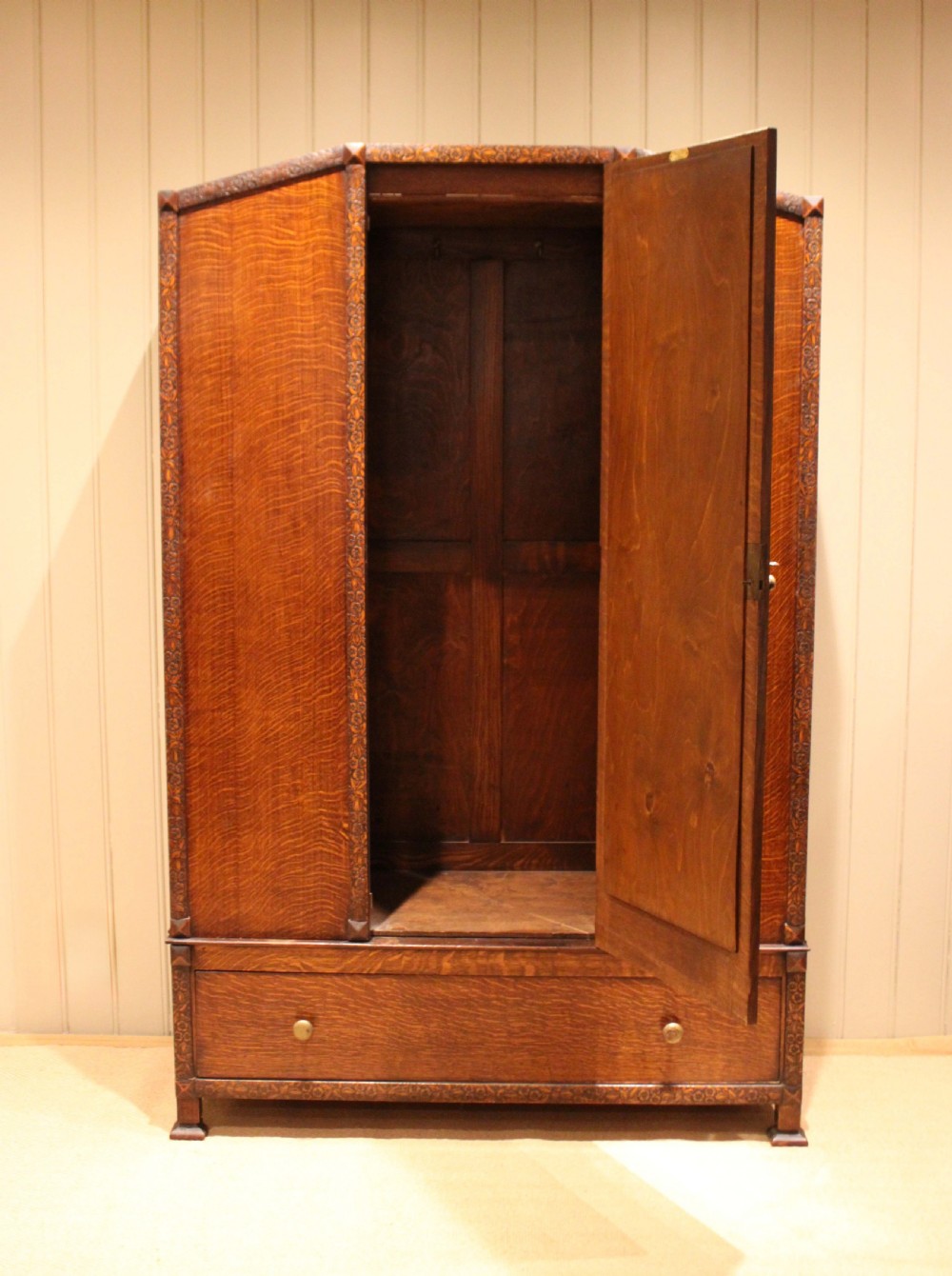 An early twentieth-century warm brown oak wardrobe with a central arched mirror door, carved foliate border mouldings, and a single lower drawer. View V
