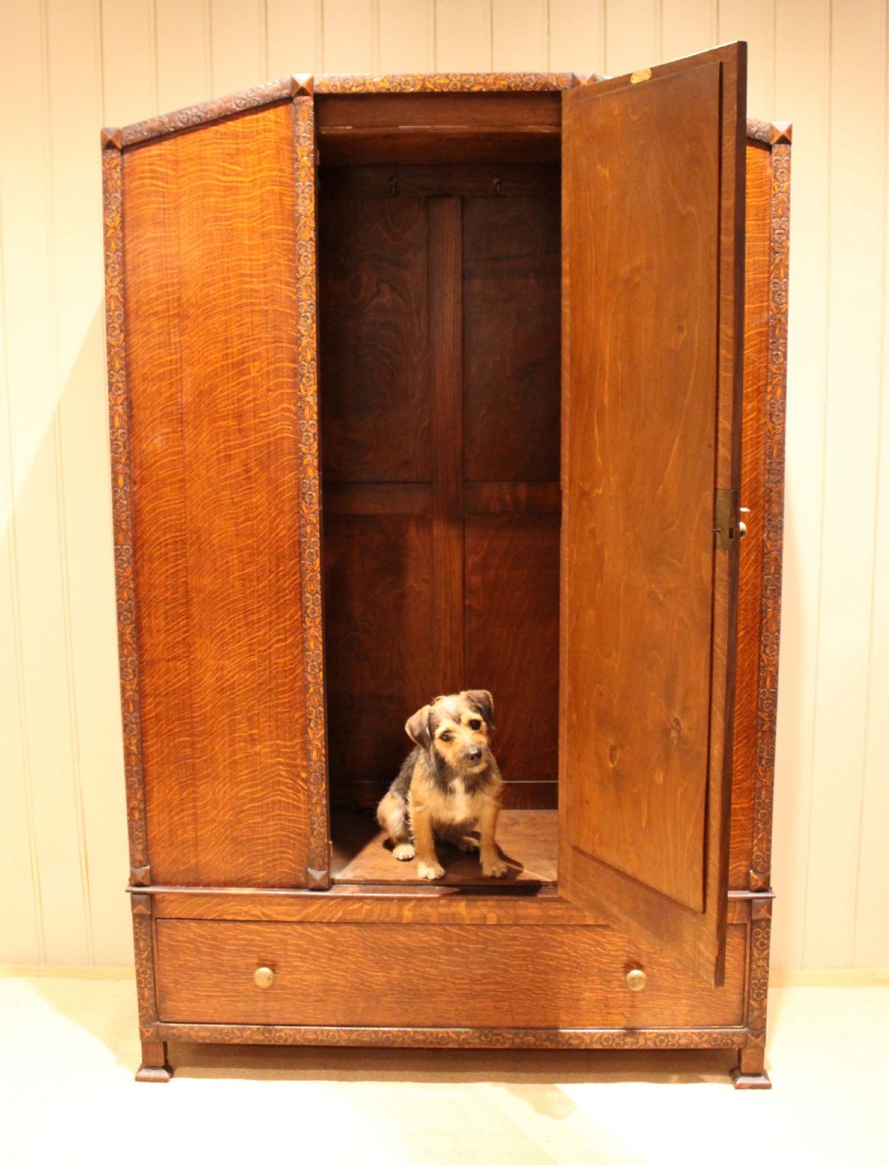 An early twentieth-century warm brown oak wardrobe with a central arched mirror door, carved foliate border mouldings, and a single lower drawer. View VI