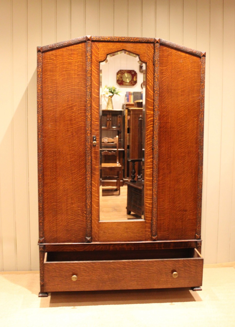 An early twentieth-century warm brown oak wardrobe with a central arched mirror door, carved foliate border mouldings, and a single lower drawer. View VII