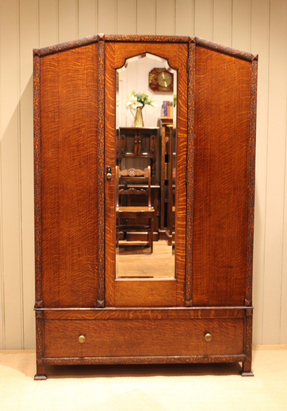 An early twentieth-century warm brown oak wardrobe with a central arched mirror door, carved foliate border mouldings, and a single lower drawer. View VIII