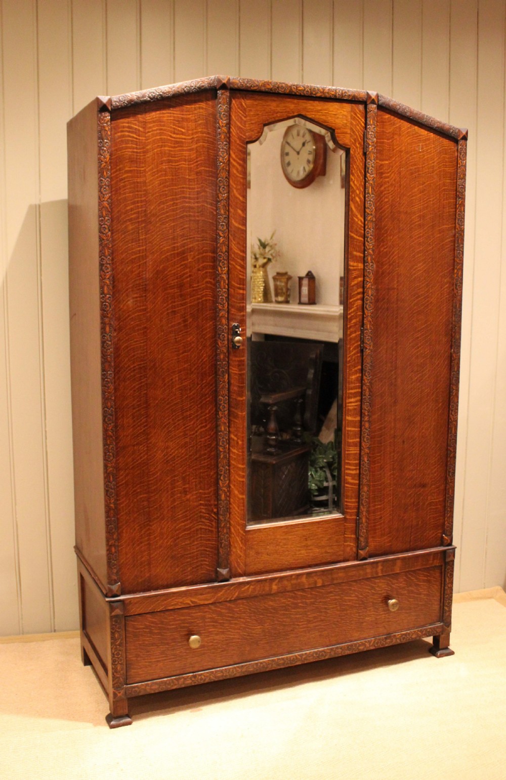 An early twentieth-century warm brown oak wardrobe with a central arched mirror door, carved foliate border mouldings, and a single lower drawer. View IX