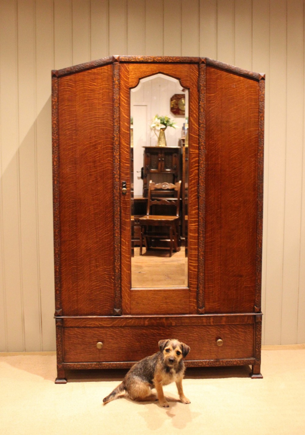 An early twentieth-century warm brown oak wardrobe with a central arched mirror door, carved foliate border mouldings, and a single lower drawer. View XI