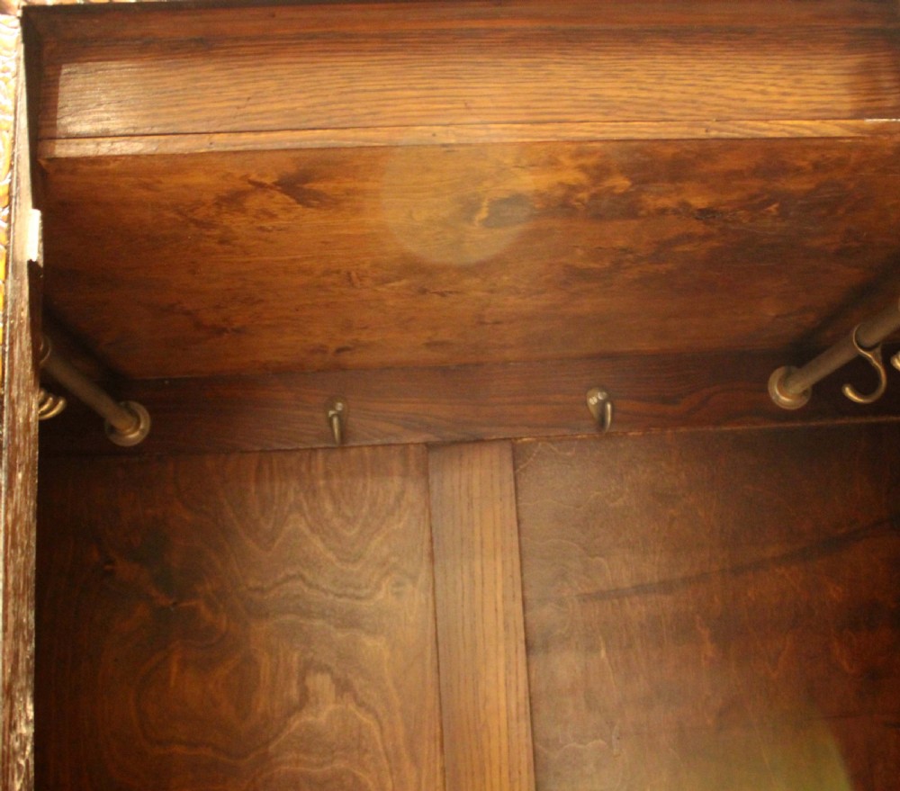 An early twentieth-century warm brown oak wardrobe with a central arched mirror door, carved foliate border mouldings, and a single lower drawer. View XII