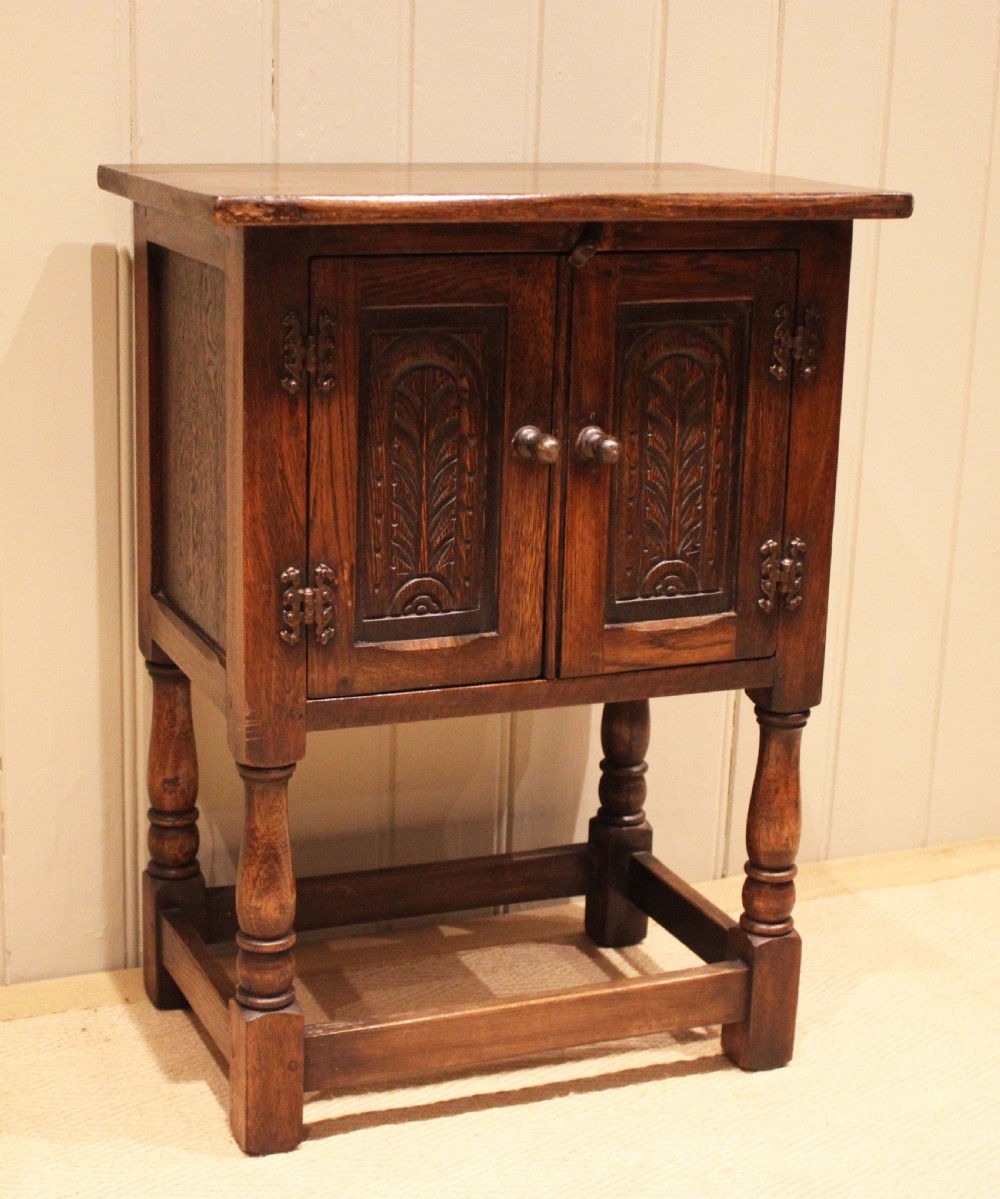A small dark oak side cabinet featuring double carved panel doors, iron hinges, turned legs, and lower wooden stretchers.
