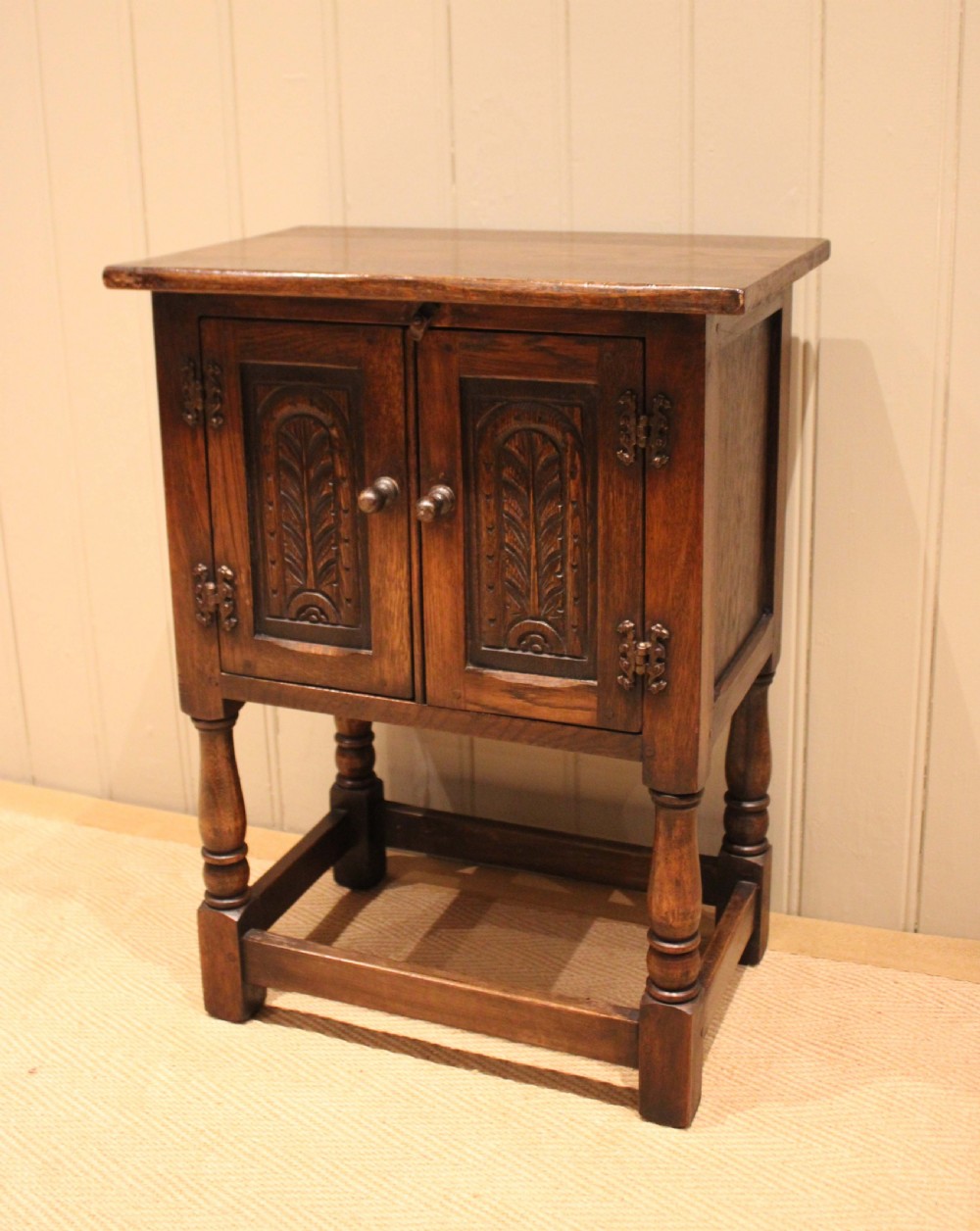 A small dark oak side cabinet featuring double carved panel doors, iron hinges, turned legs, and lower wooden stretchers. View II