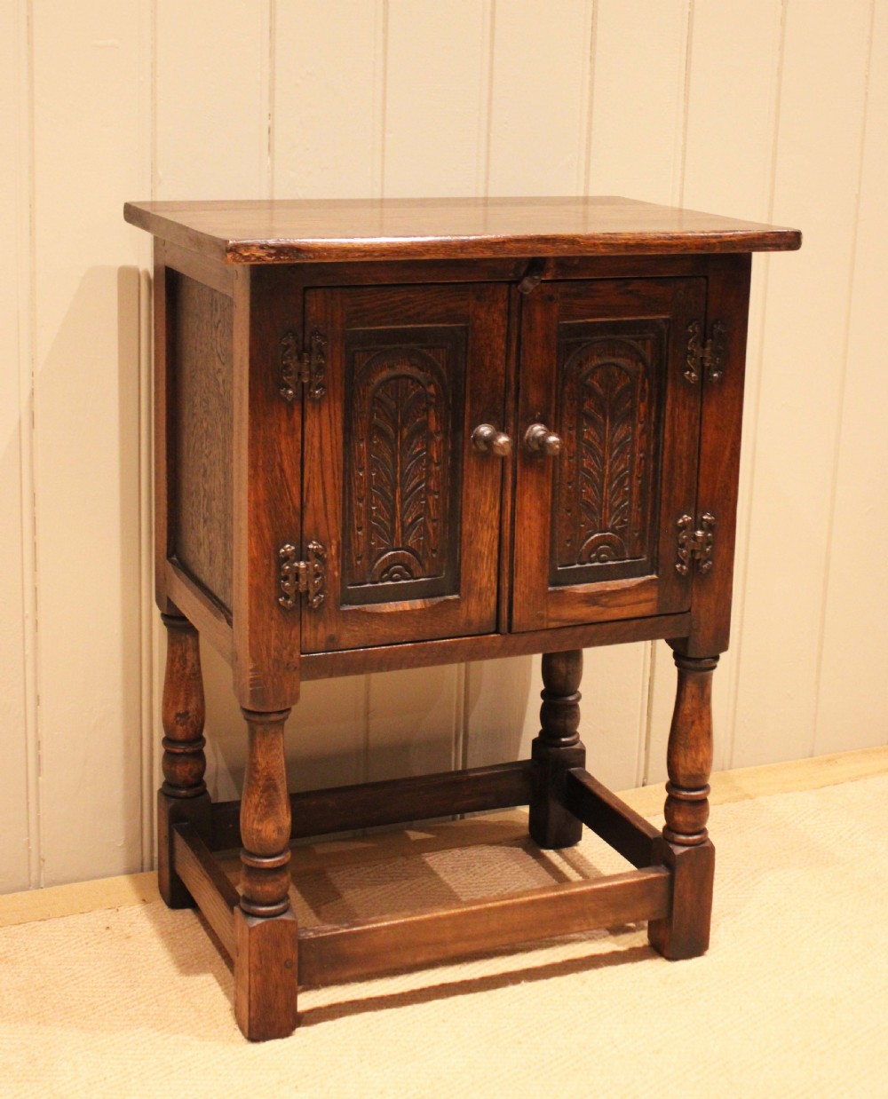 A small dark oak side cabinet featuring double carved panel doors, iron hinges, turned legs, and lower wooden stretchers. View IV