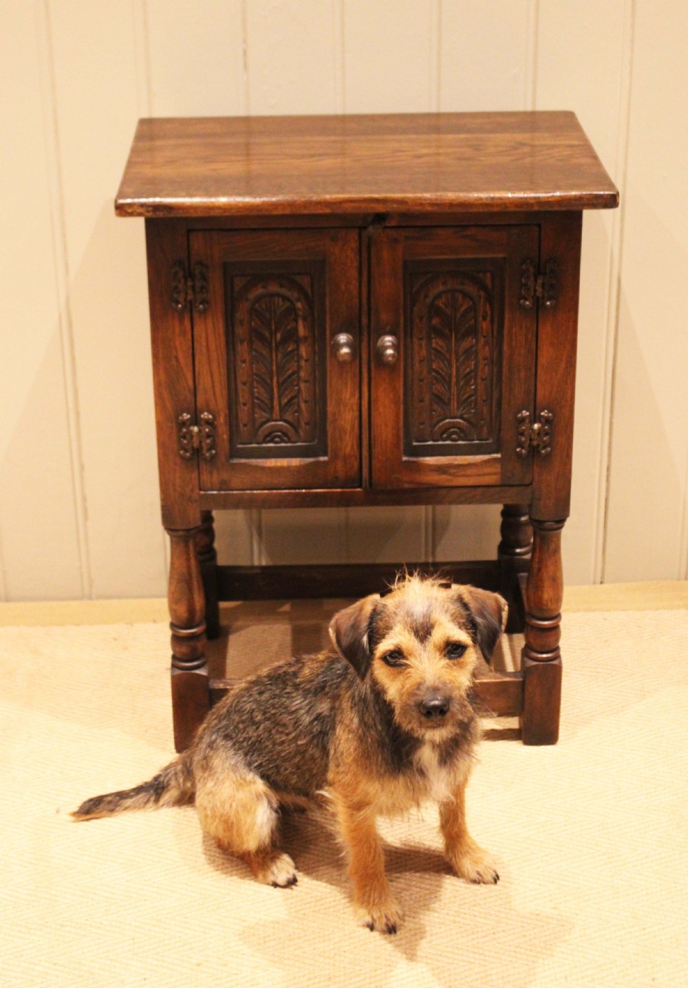 A small dark oak side cabinet featuring double carved panel doors, iron hinges, turned legs, and lower wooden stretchers. View VI