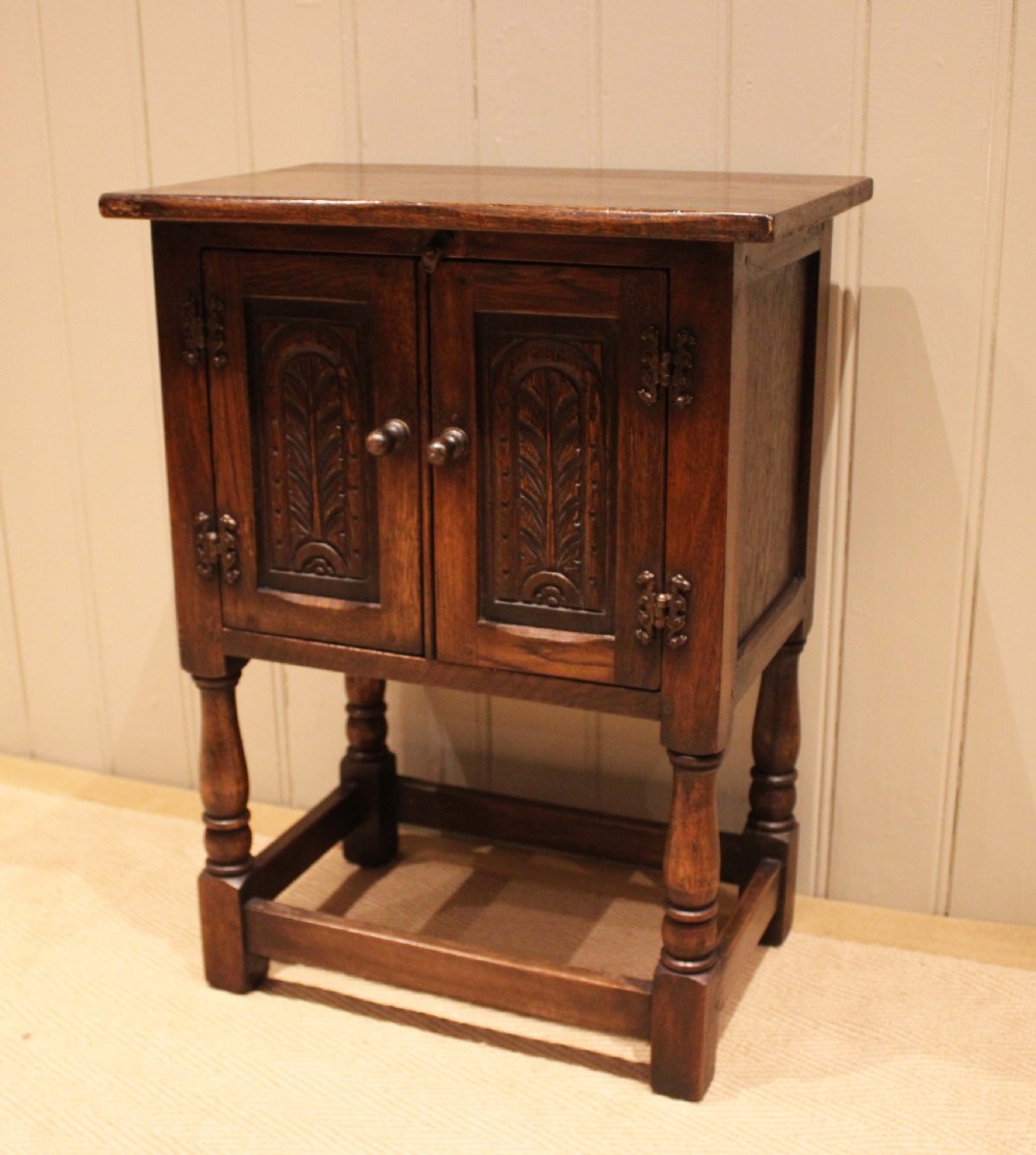 A small dark oak side cabinet featuring double carved panel doors, iron hinges, turned legs, and lower wooden stretchers. View VII