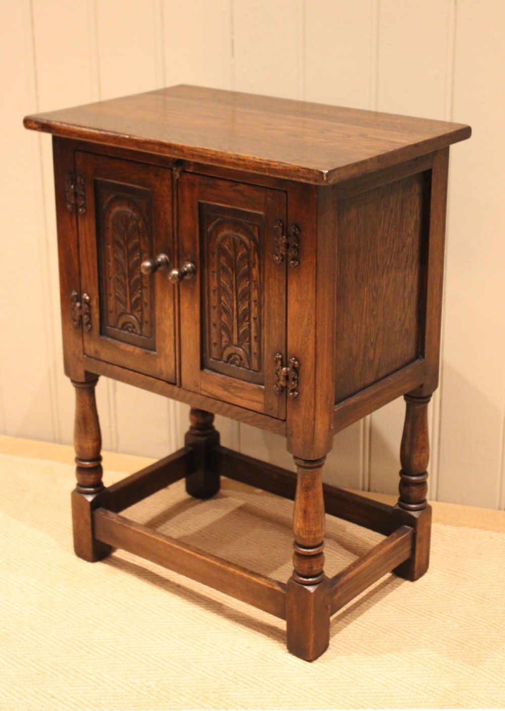 A small dark oak side cabinet featuring double carved panel doors, iron hinges, turned legs, and lower wooden stretchers. View VIII