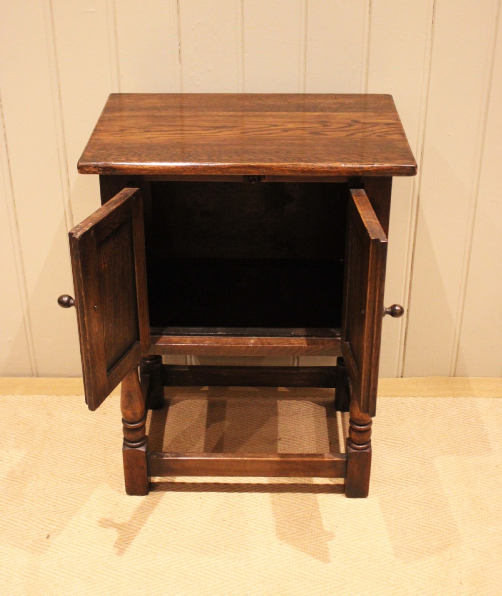 A small dark oak side cabinet featuring double carved panel doors, iron hinges, turned legs, and lower wooden stretchers. View IX