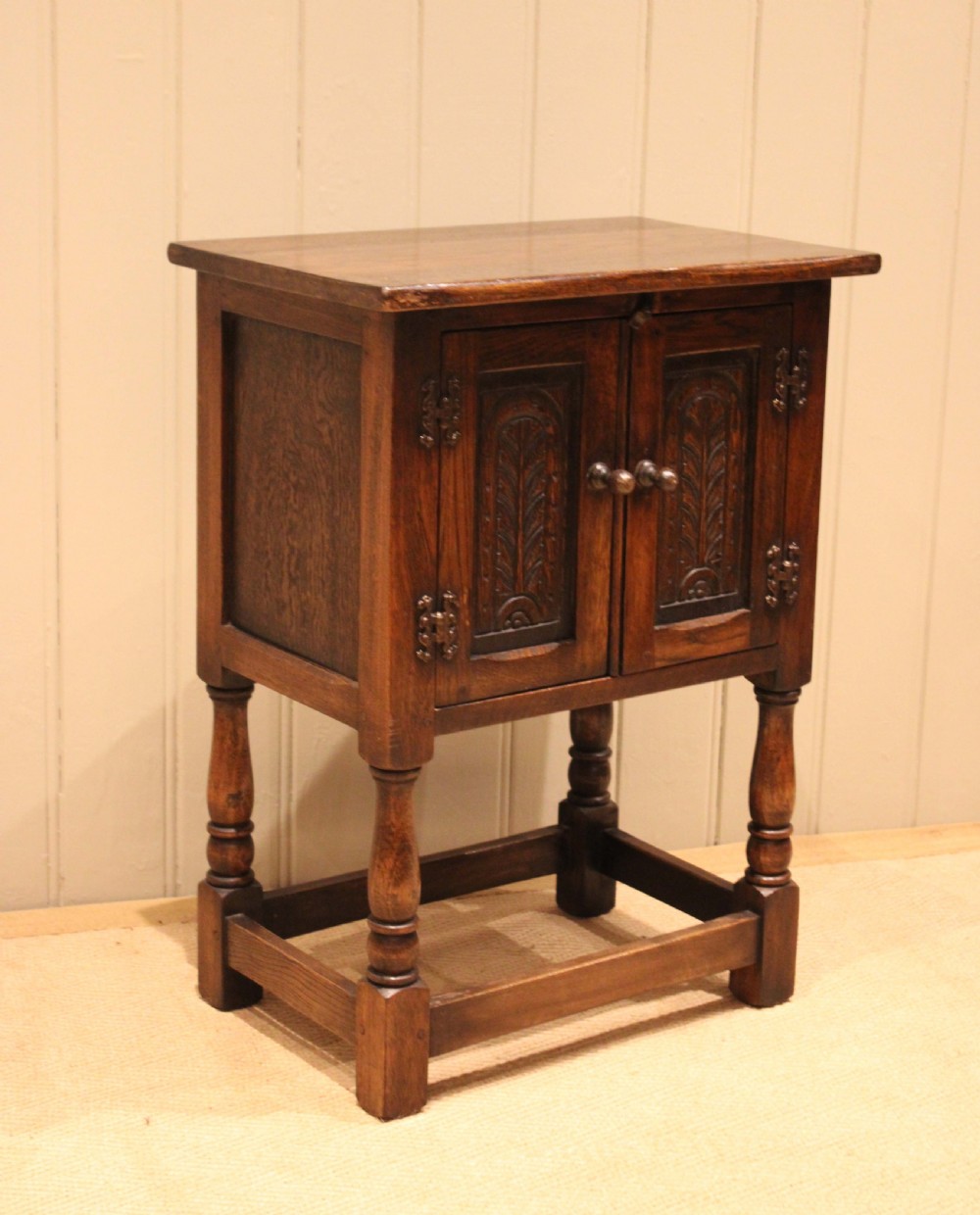 A small dark oak side cabinet featuring double carved panel doors, iron hinges, turned legs, and lower wooden stretchers. View X