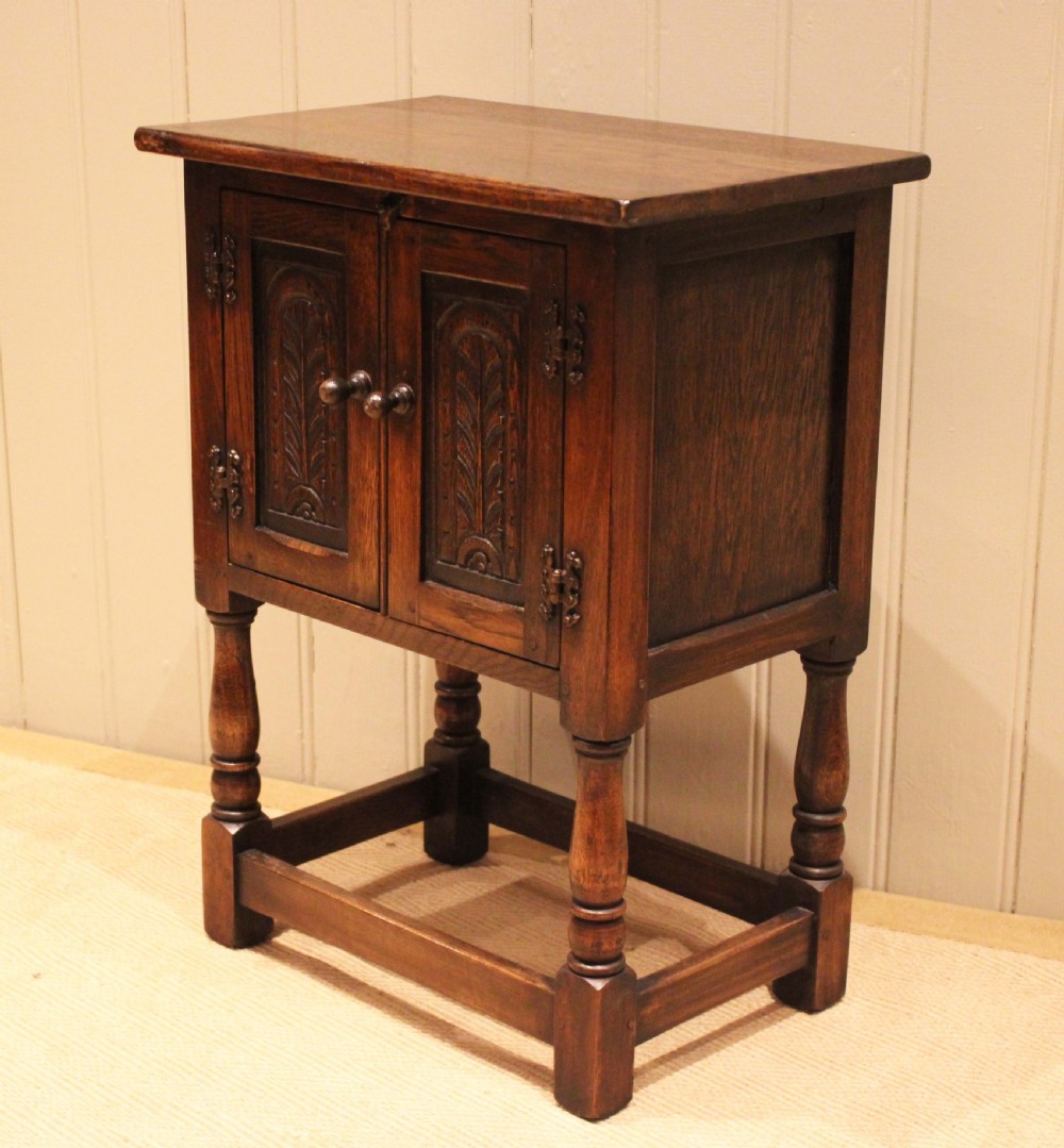 A small dark oak side cabinet featuring double carved panel doors, iron hinges, turned legs, and lower wooden stretchers. View XI